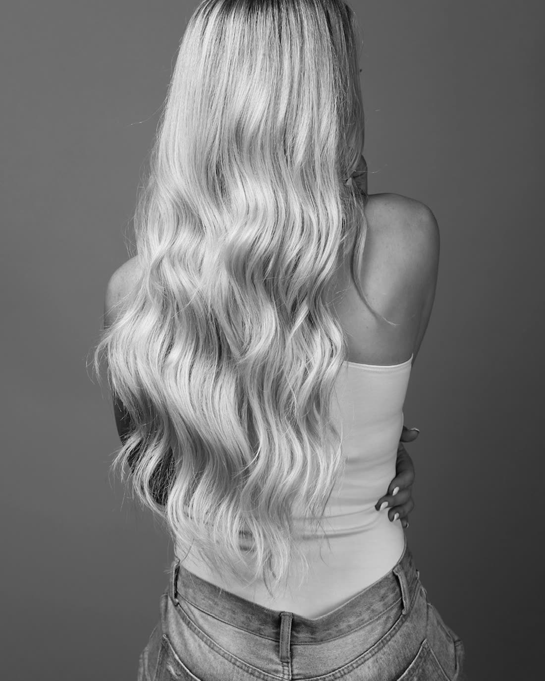Long blonde tape-in extensions, waved and worn to the waist, photographed from behind in studio